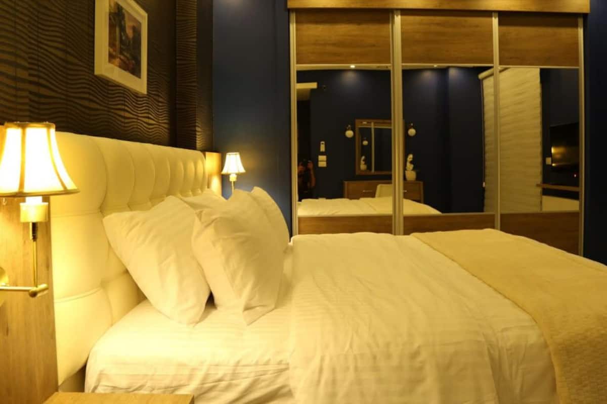 A hotel room with a large bed, two bedside lamps, a mirror, and a wooden headboard.