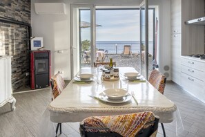 Uma sala de jantar com vista para o mar, uma cozinha com fogão e uma geladeira.