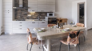 A modern kitchen with a central island, built-in appliances, and a dining area with patterned chairs. - Casa Ciapin (Cipressa)