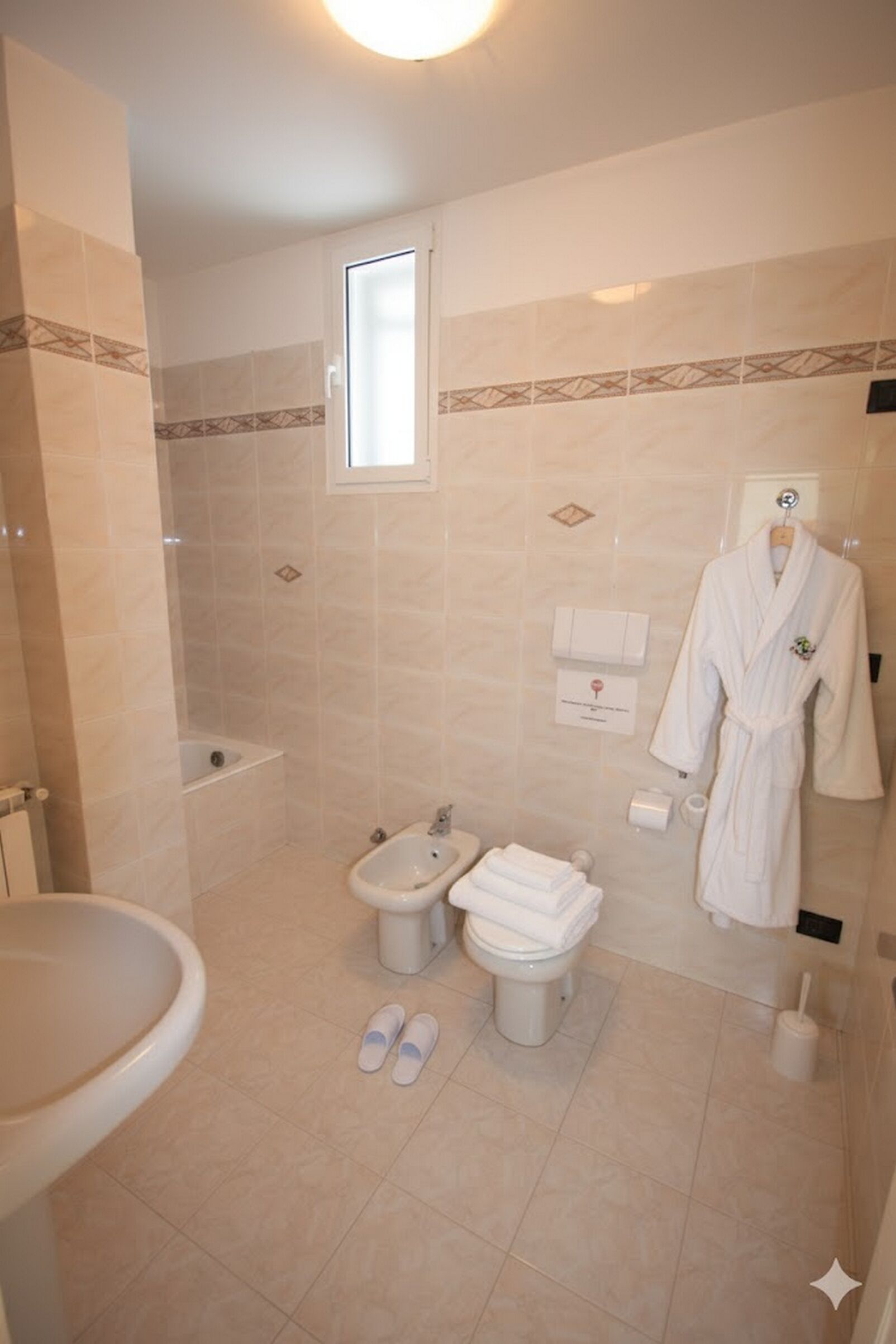 A bathroom with a bathtub, bidet, toilet, and a robe hanging on the wall.