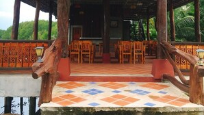 A covered outdoor seating area with wooden chairs and tables, a tiled floor, and a red roof. - Bussarin Mansion (Ko Yao)