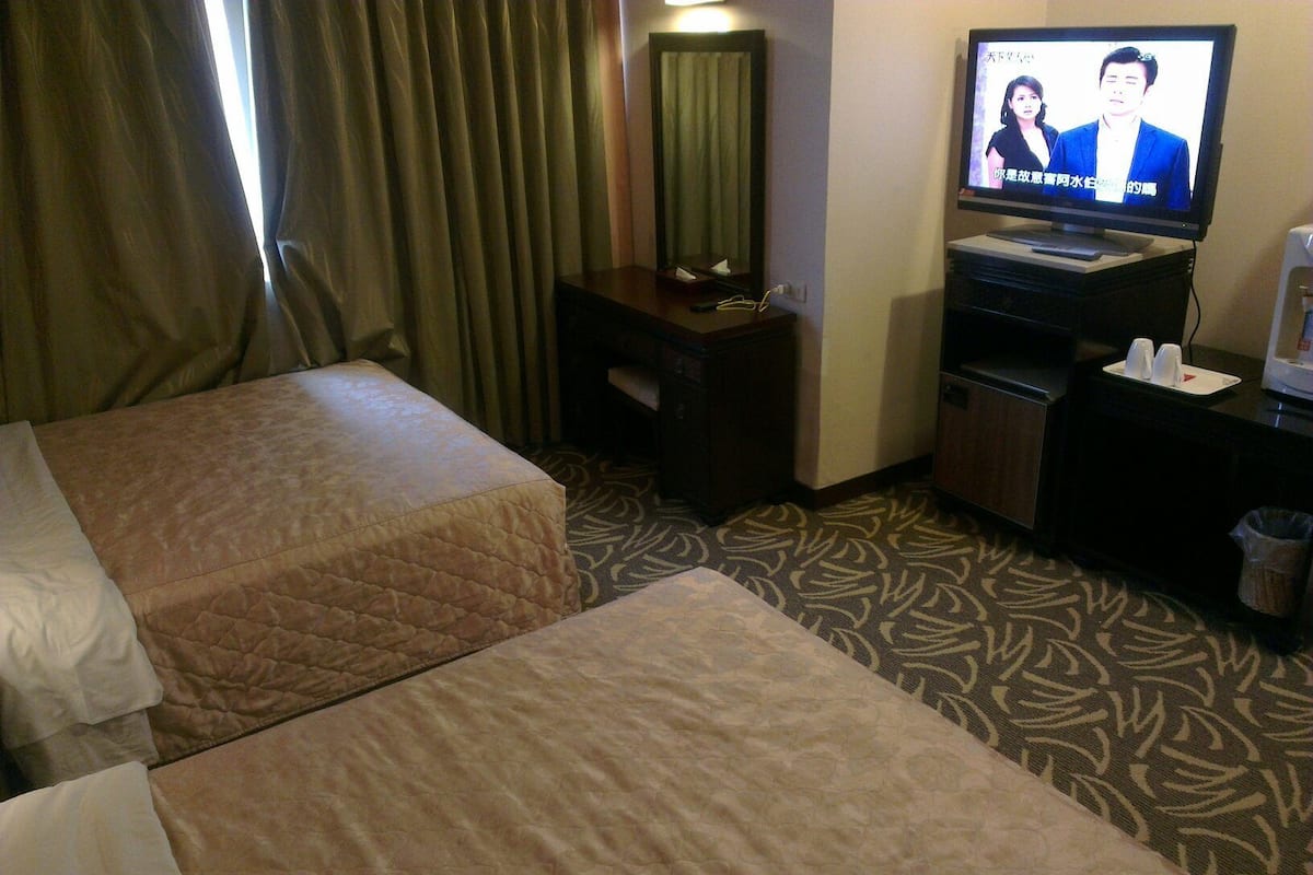 A hotel room with two beds, a television, a small table, and a trash bin.
