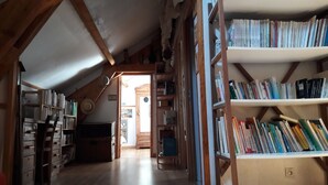Un acogedor dormitorio en el ático con vigas de madera, una estantería llena de libros y un pequeño escritorio.