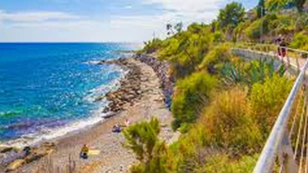 A coastal road with a rocky shoreline, greenery, and a clear blue sky. - Casa Airenti (Imperia)
