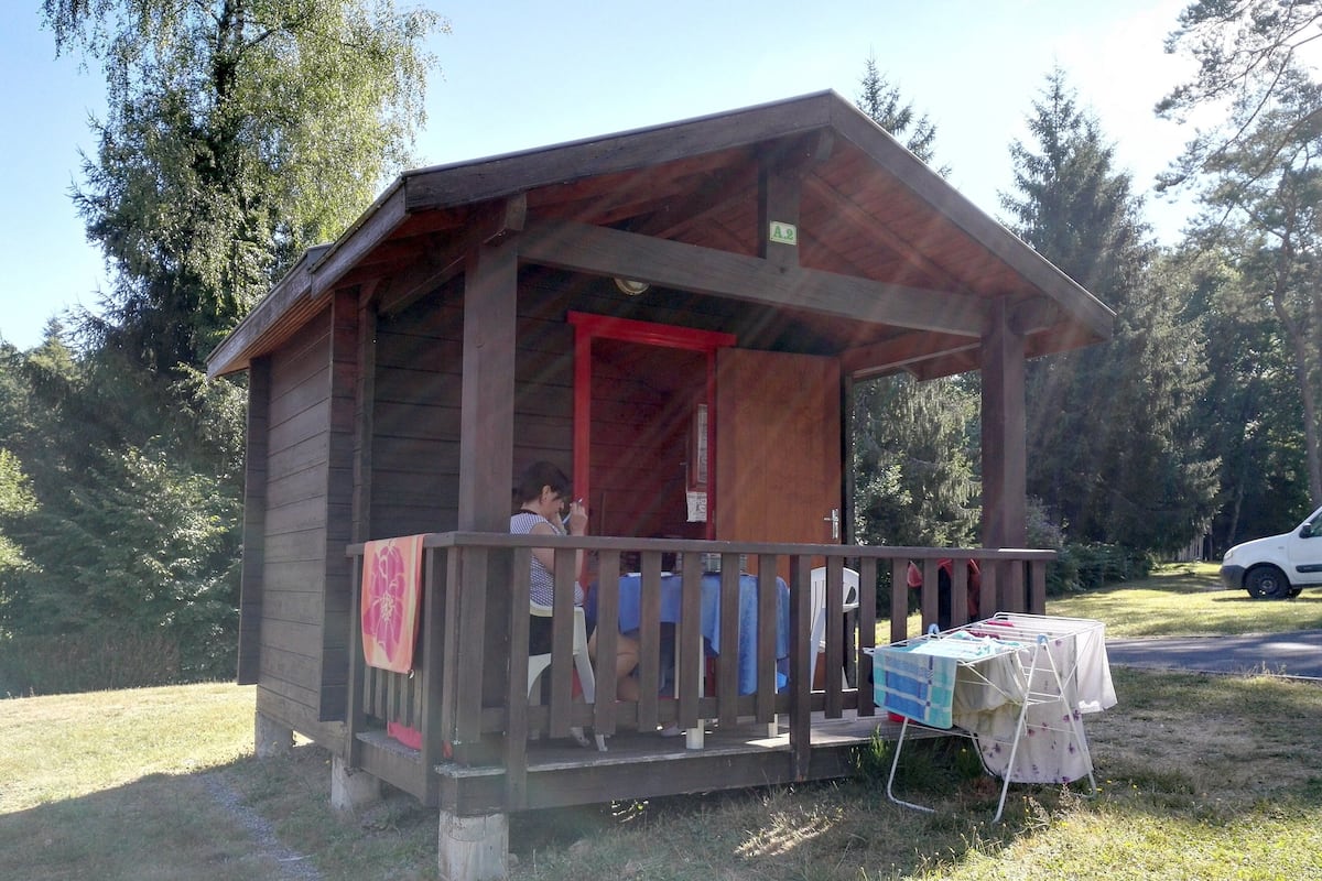 Une cabane en bois avec une véranda, une table recouverte d’une nappe et une voiture garée à proximité.