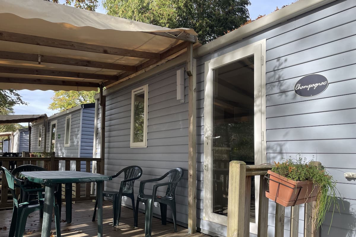 Un espace extérieur aménagé, abrité et doté d’une table et de chaises, d’une terrasse en bois et d’une enseigne indiquant « Champagnac ».