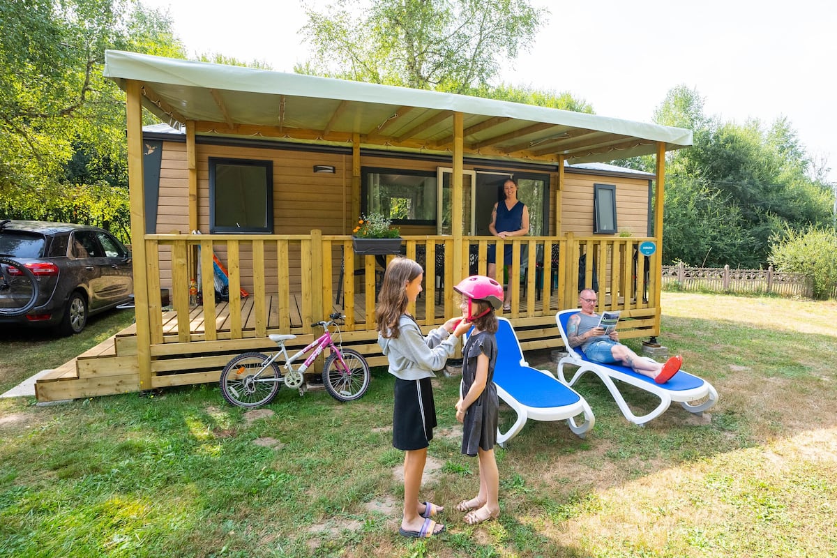 Une cabane en bois avec un porche, un vélo et une voiture garée à proximité.