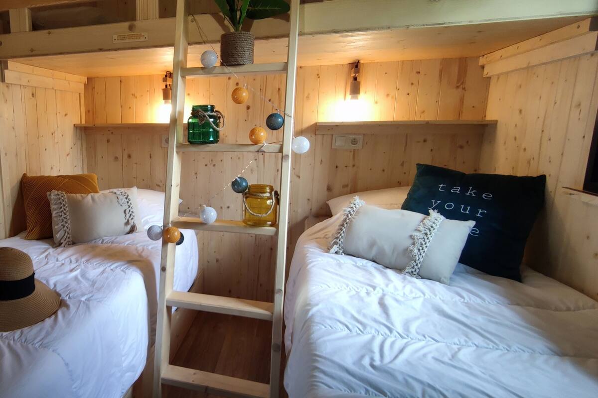 Une chambre confortable, aménagée comme un chalet, avec deux lits, des murs en bois, une échelle et une étagère où sont posés des bocaux et des ballons.