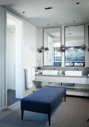 A modern bathroom with two sinks, a large mirror, and a bench.