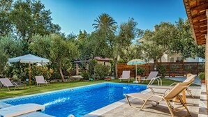 A backyard with a swimming pool, lounge chairs, and a wooden deck. - Kardaris Villa (Zakynthos)