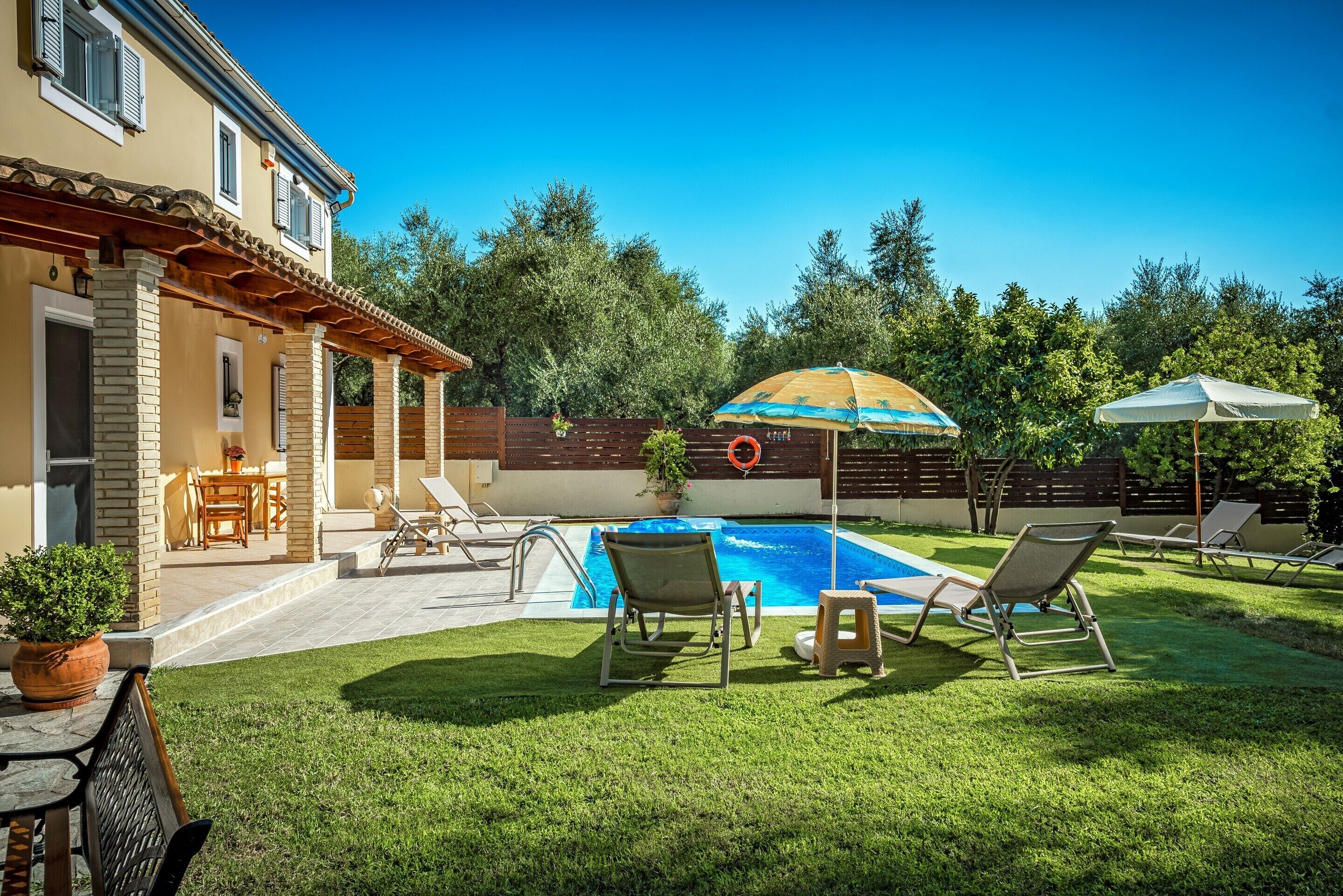 Un patio trasero con piscina, sillas de descanso, una pérgola y una terraza de madera.