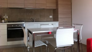 A modern kitchen with wooden cabinets, a stainless steel stove, and a dining area with a white table and chairs. - Affittacamere Nonna Leni (Frisanco)