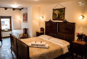 Une chambre d’hôtel avec un grand lit, une armoire en bois, une table de chevet avec une lampe, une fenêtre donnant sur des fleurs et un tableau au mur.