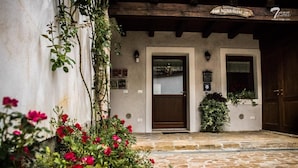 A building with a stone facade, two wooden doors, and a small garden with pink flowers. - Affittacamere Nonna Leni (Frisanco)