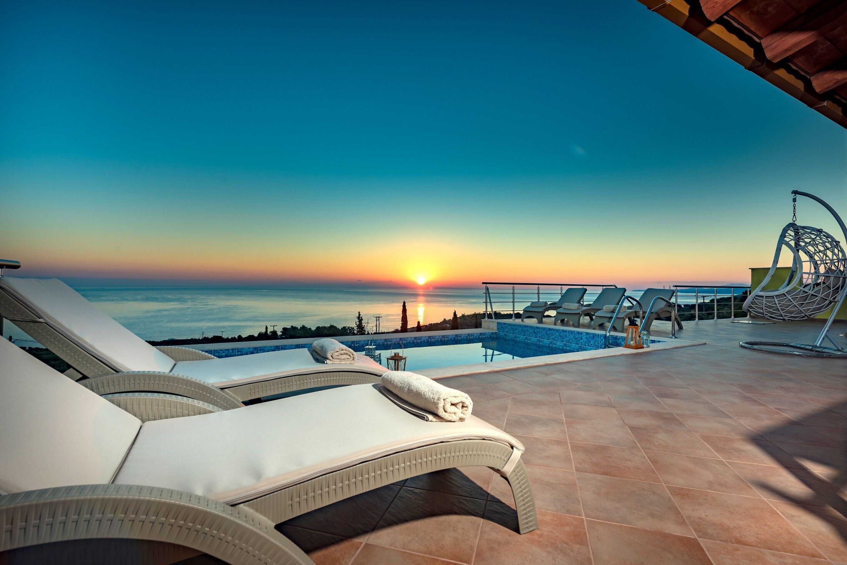 A poolside area with lounge chairs and a view of the sunset over the ocean.
