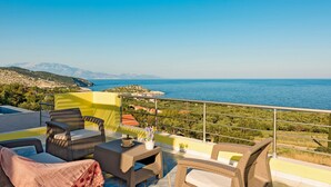 Ein Balkon mit Korbmöbeln, einer Topfpflanze und Blick auf das Meer und die Berge.