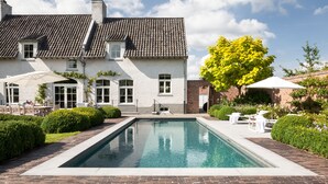 Een zwembadterras met een wit gebouw, een zwembad en buitengelegen zitplaatsen.