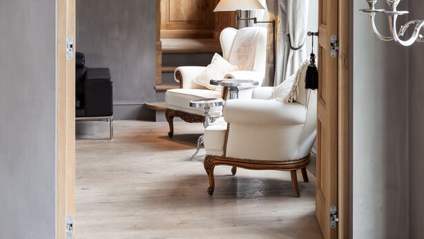Een kamer met een houten boog die leidt naar een zithoek met een bank en fauteuils, een lamp en een wandlamp.