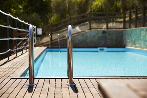 Una terraza de madera con barandas metálicas junto a la piscina y una piscina azul cristalina.