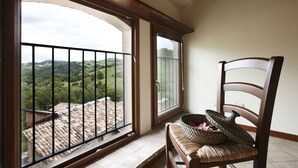 A balcony with a view of green hills and a tiled roof.