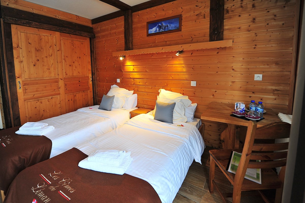 Una habitación de cabaña de madera con dos camas, una mesa de madera con botellas de agua y un cuadro en la pared.
