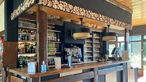 A bar area with wooden shelves stocked with bottles and glasses, a coffee machine, and a cash register. - Les Cimes du Léman (Habere-Poche)
