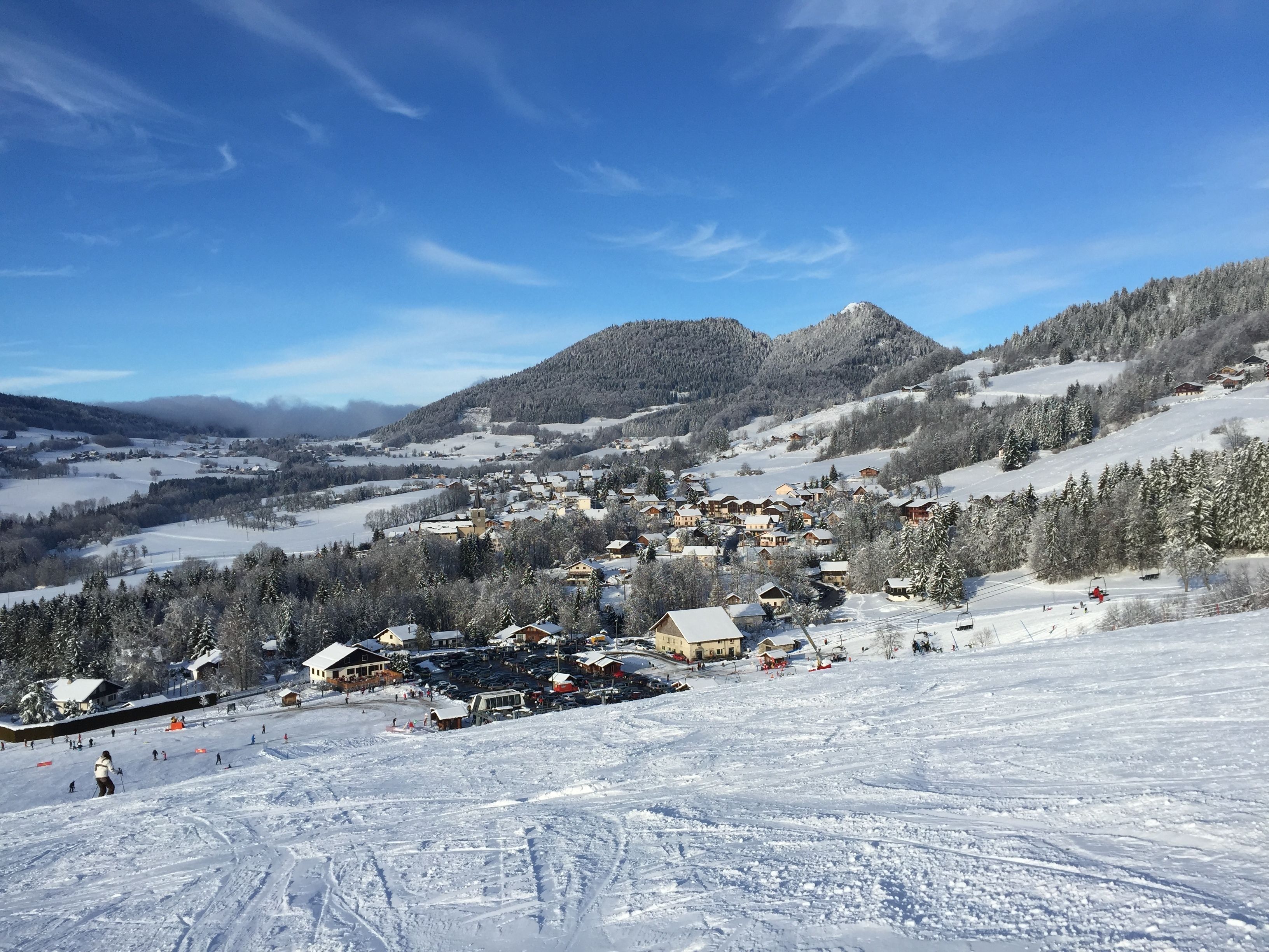 A snow-covered ski resort with buildings, ski slopes, and a mountain backdrop.