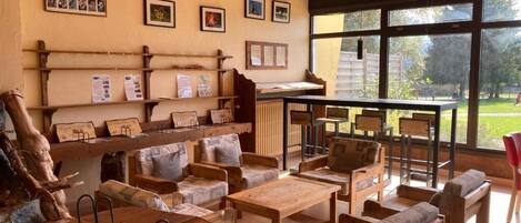 A cozy room with wooden furniture, a large window, and a bulletin board with photos and notices.