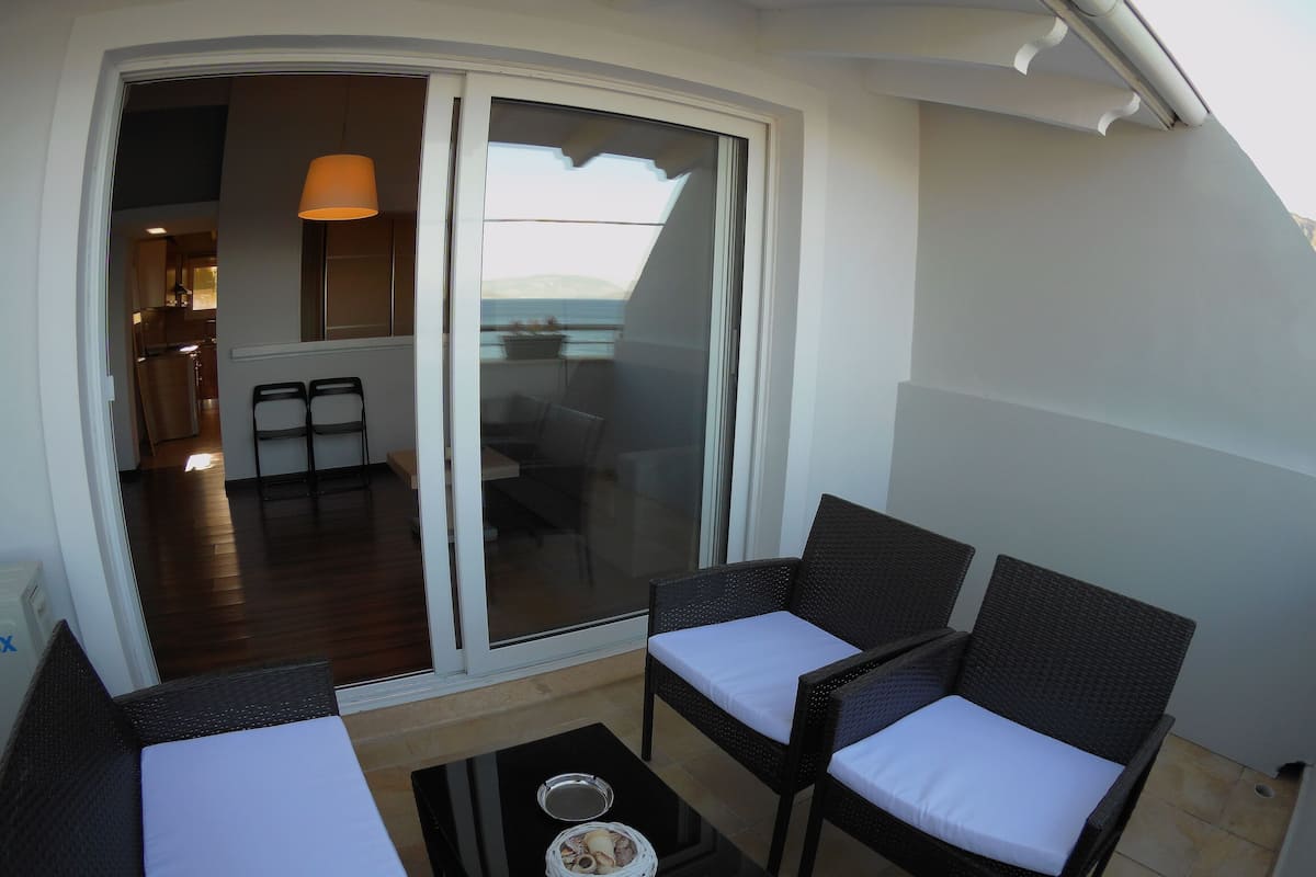 A balcony with wicker furniture and a glass door leading to an interior space.