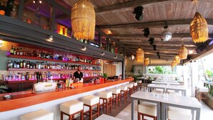 A bar area with a long counter, multiple stools, and a variety of bottles and glasses. - Onar Corfu Aparts & Studios (Corfu)