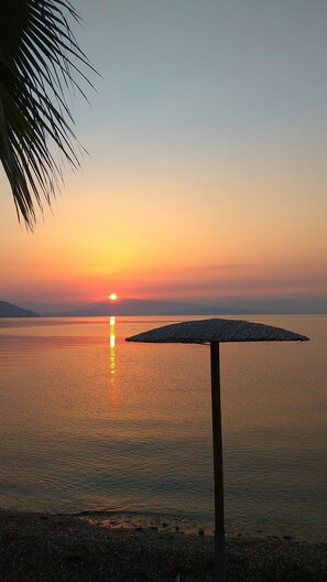 A sunset over a calm body of water with a beach umbrella in the foreground. - Onar Corfu Aparts & Studios (Corfu)