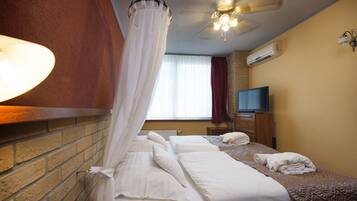 A hotel room with a brick wall, a bed with white linens, a television, and a ceiling fan.