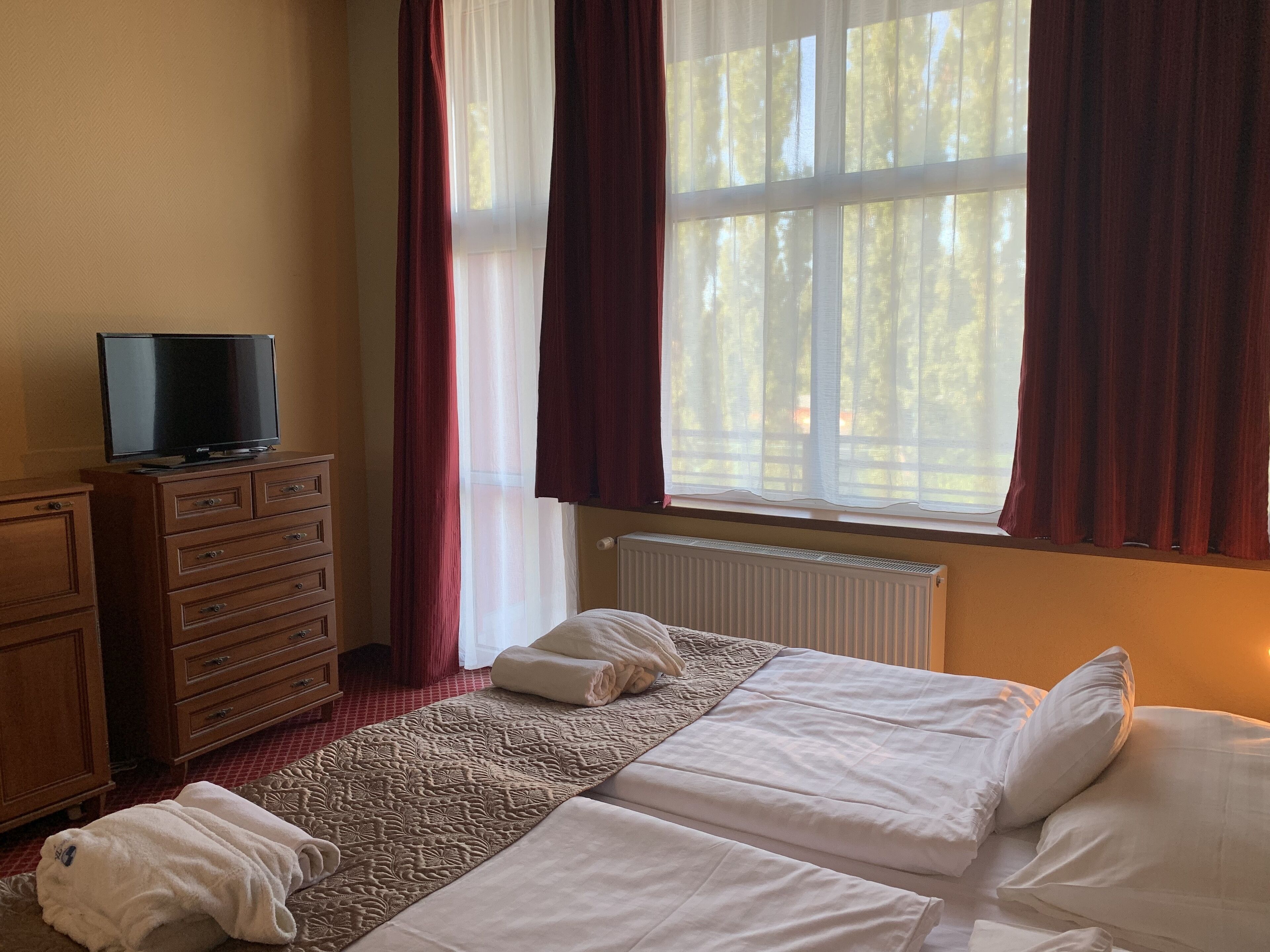 A hotel room with a bed, a TV on a dresser, and a window with curtains.