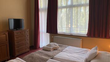 A hotel room with a bed, a TV on a dresser, and a window with curtains.