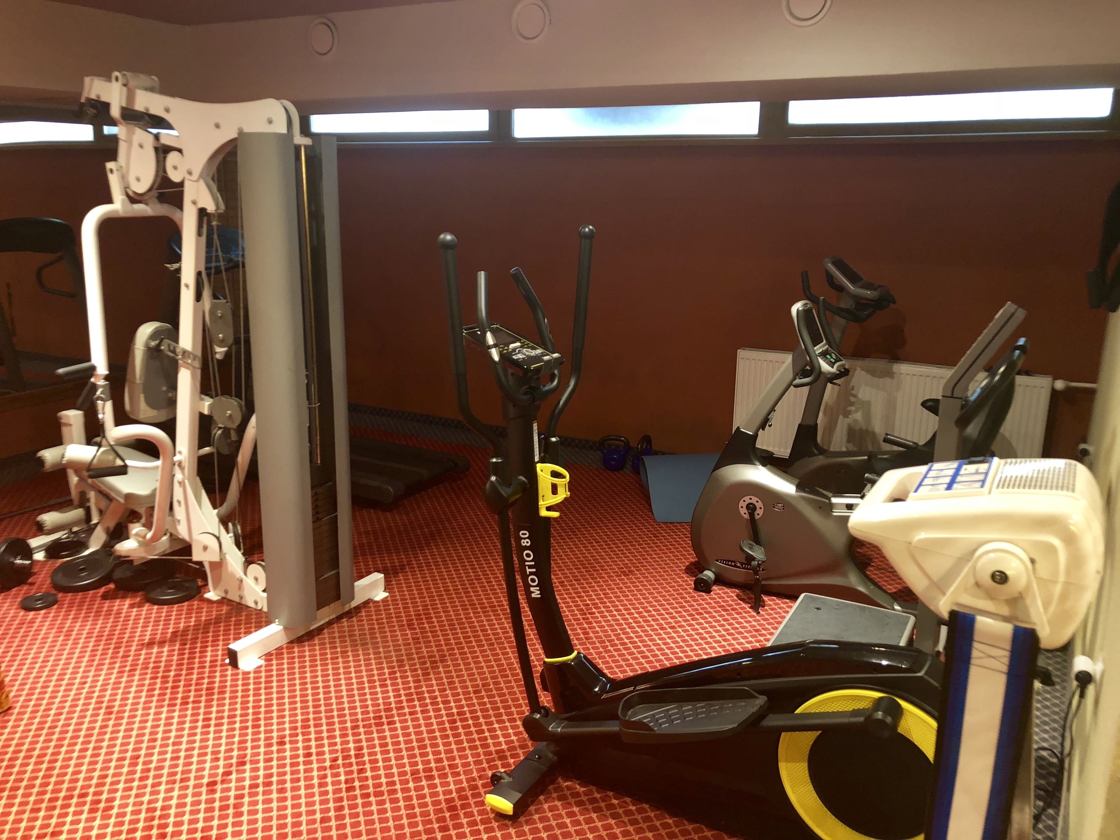 A gym with exercise equipment including a stationary bike, elliptical, and weight machines.