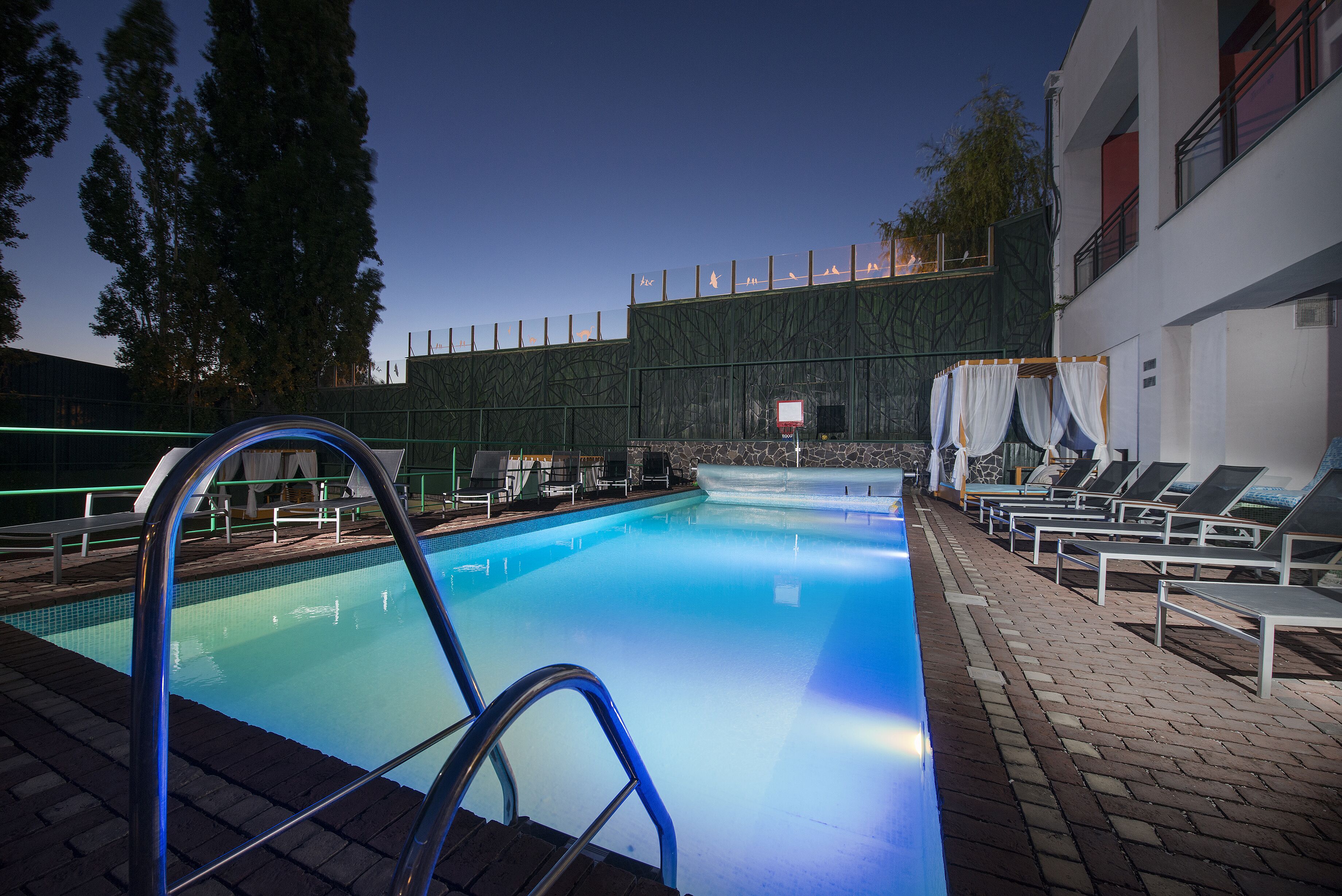 A swimming pool with a metal ladder, lounge chairs, and a covered area with a view of the pool.