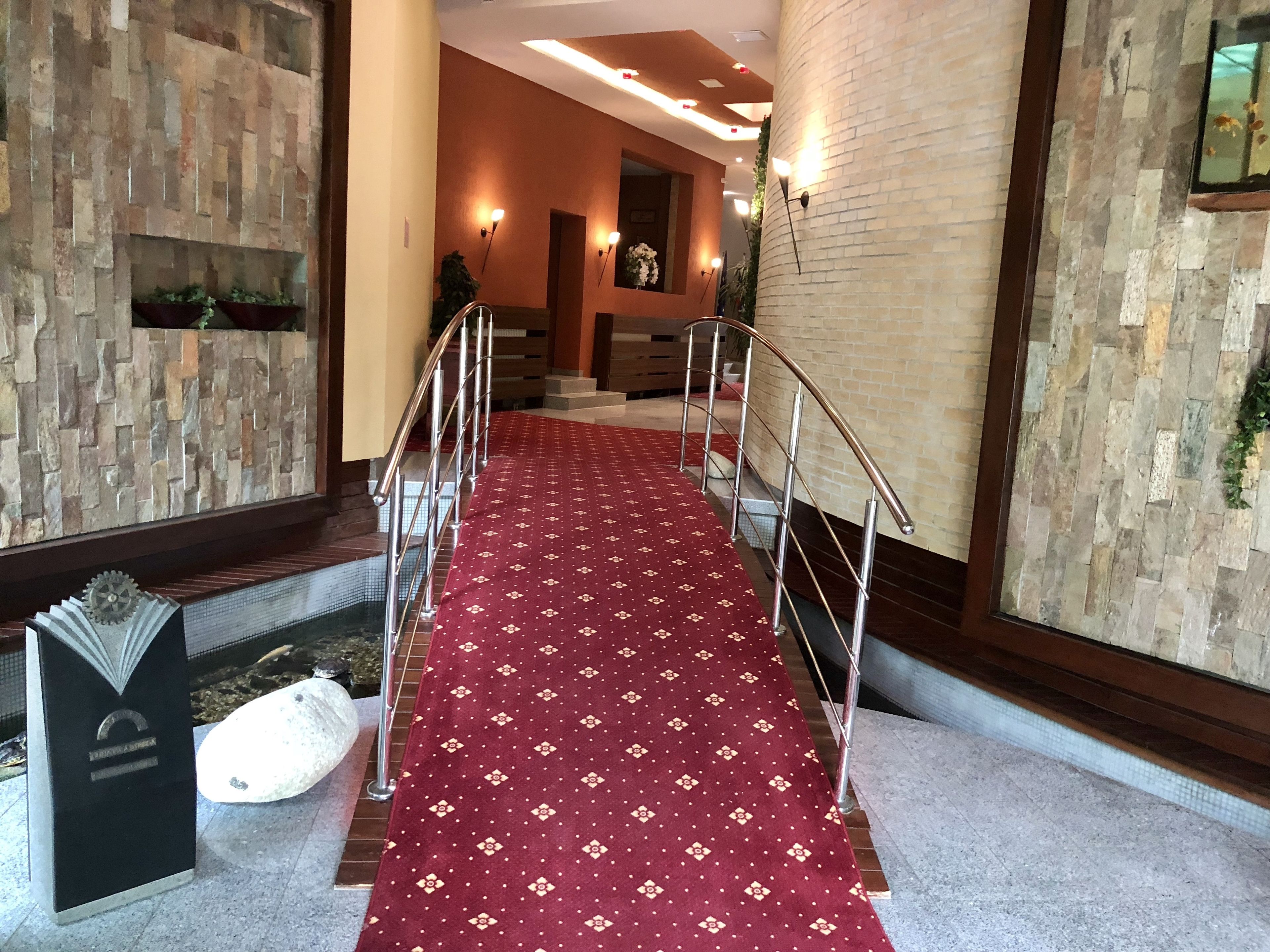 A hotel lobby with a red carpet, stone walls, and a staircase.