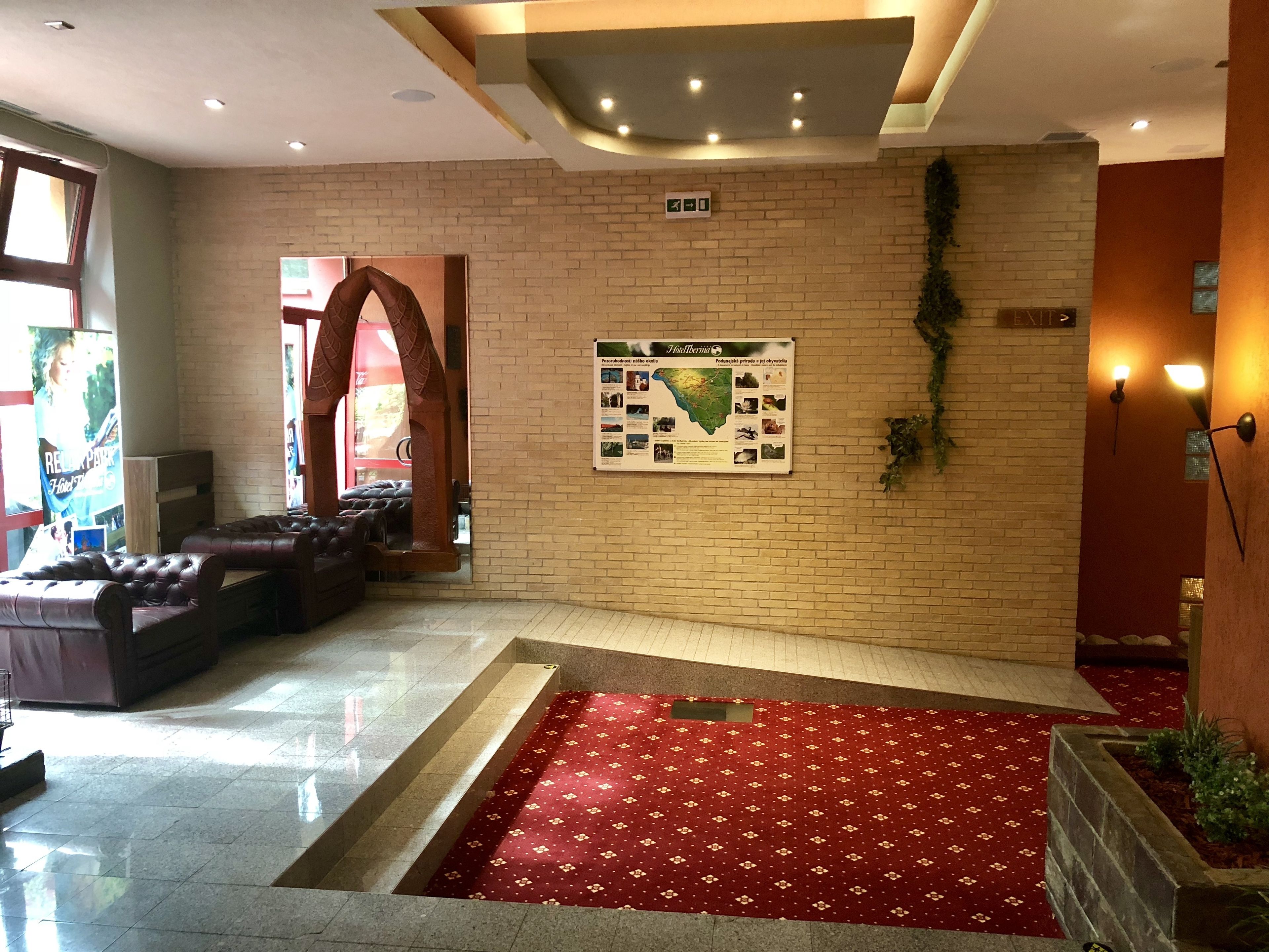 A lobby with a red carpet, leather seating, a brick wall, and a map display.
