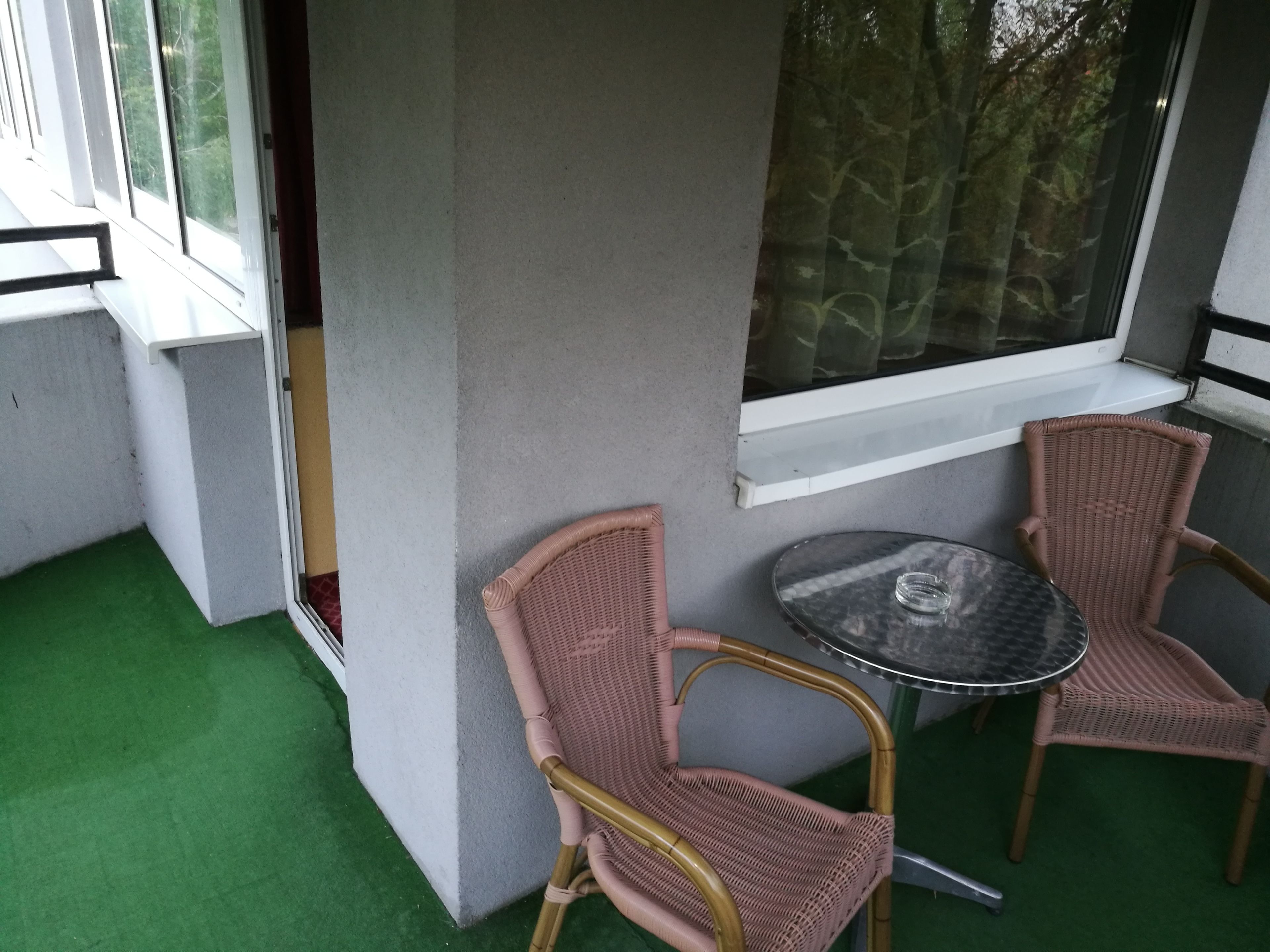 A balcony with two wicker chairs and a small round table.