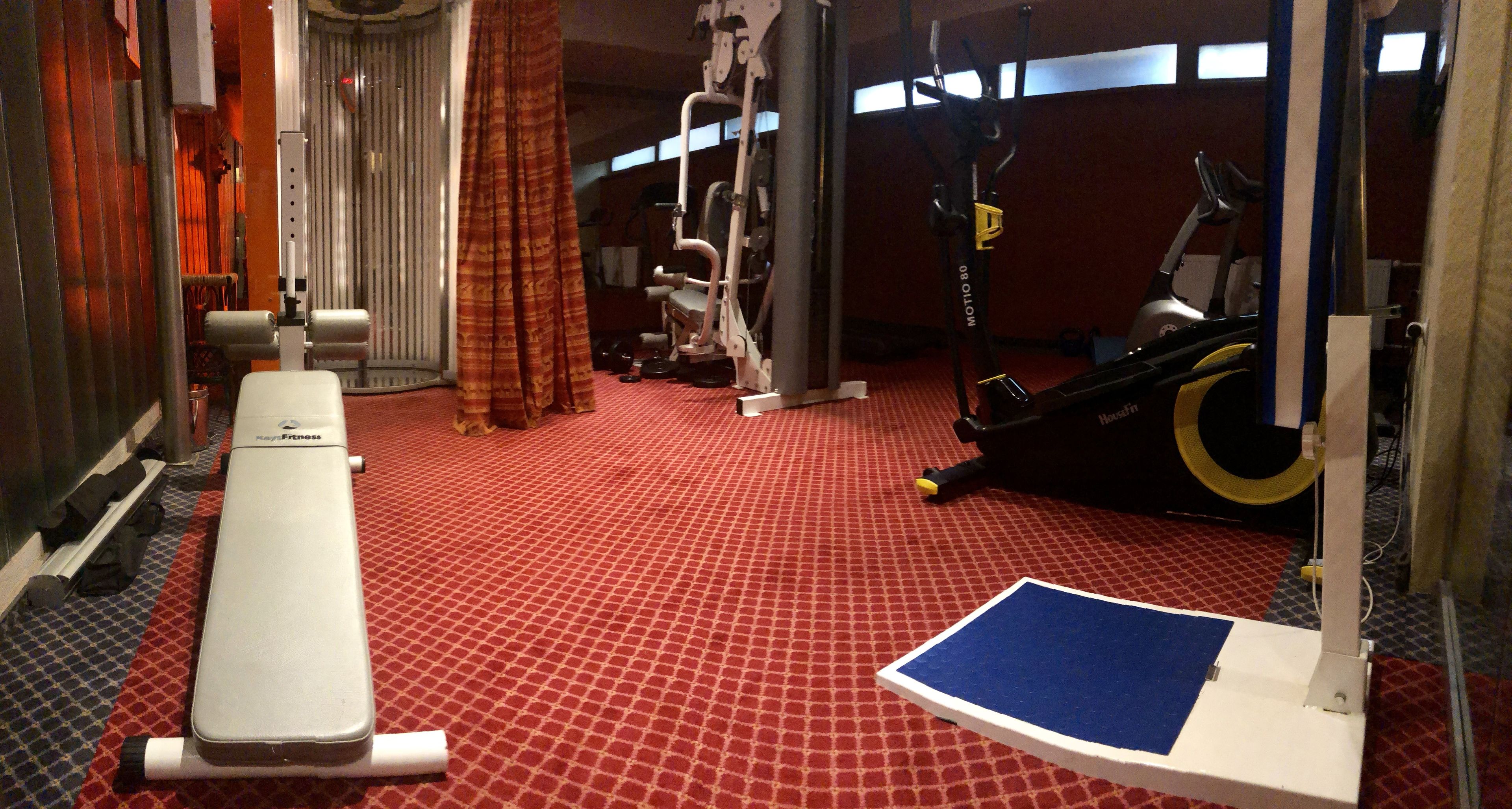 A gym with a red patterned floor, a bench, a rowing machine, and a stationary bike.