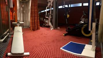 A gym with a red patterned floor, a bench, a rowing machine, and a stationary bike.