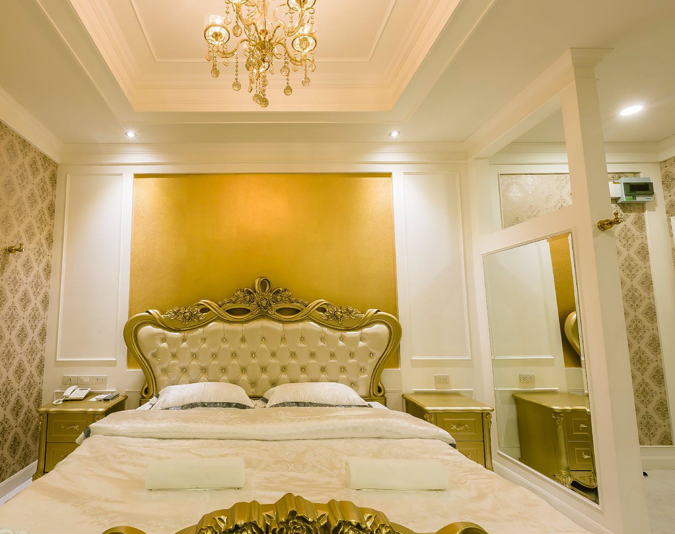 A luxurious bedroom with a large bed, a chandelier, and a mirror.