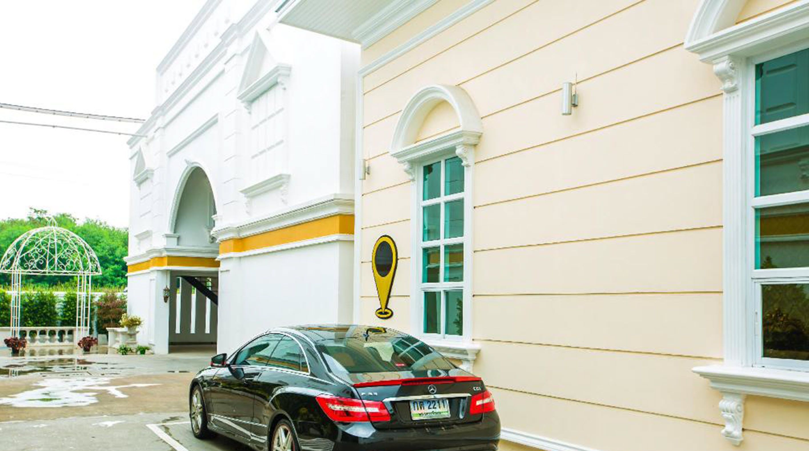 A black car parked in front of a building with a yellow and white facade, a large window, and a yellow location marker.