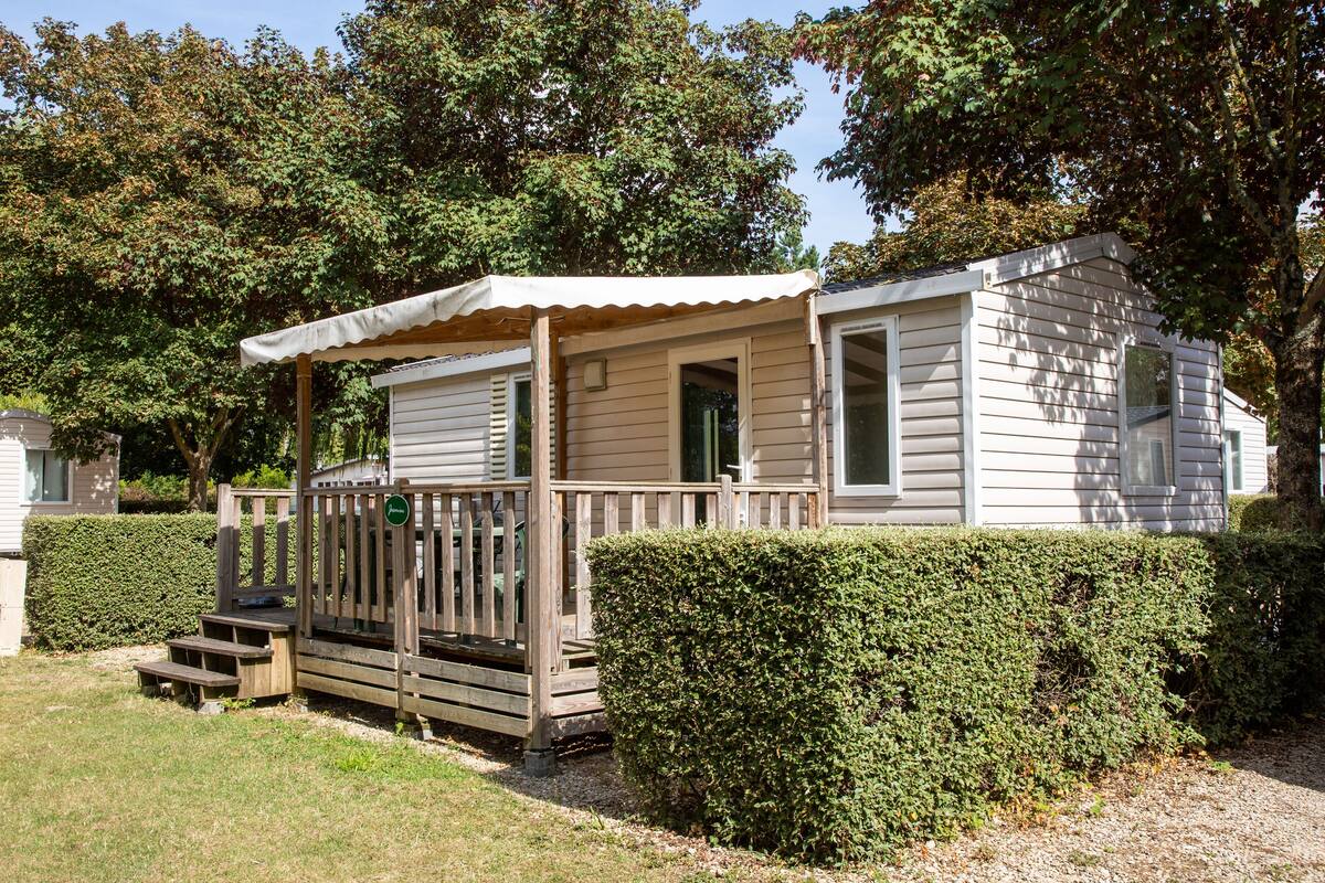 A small, single-story mobile home with a porch and a wooden deck.
