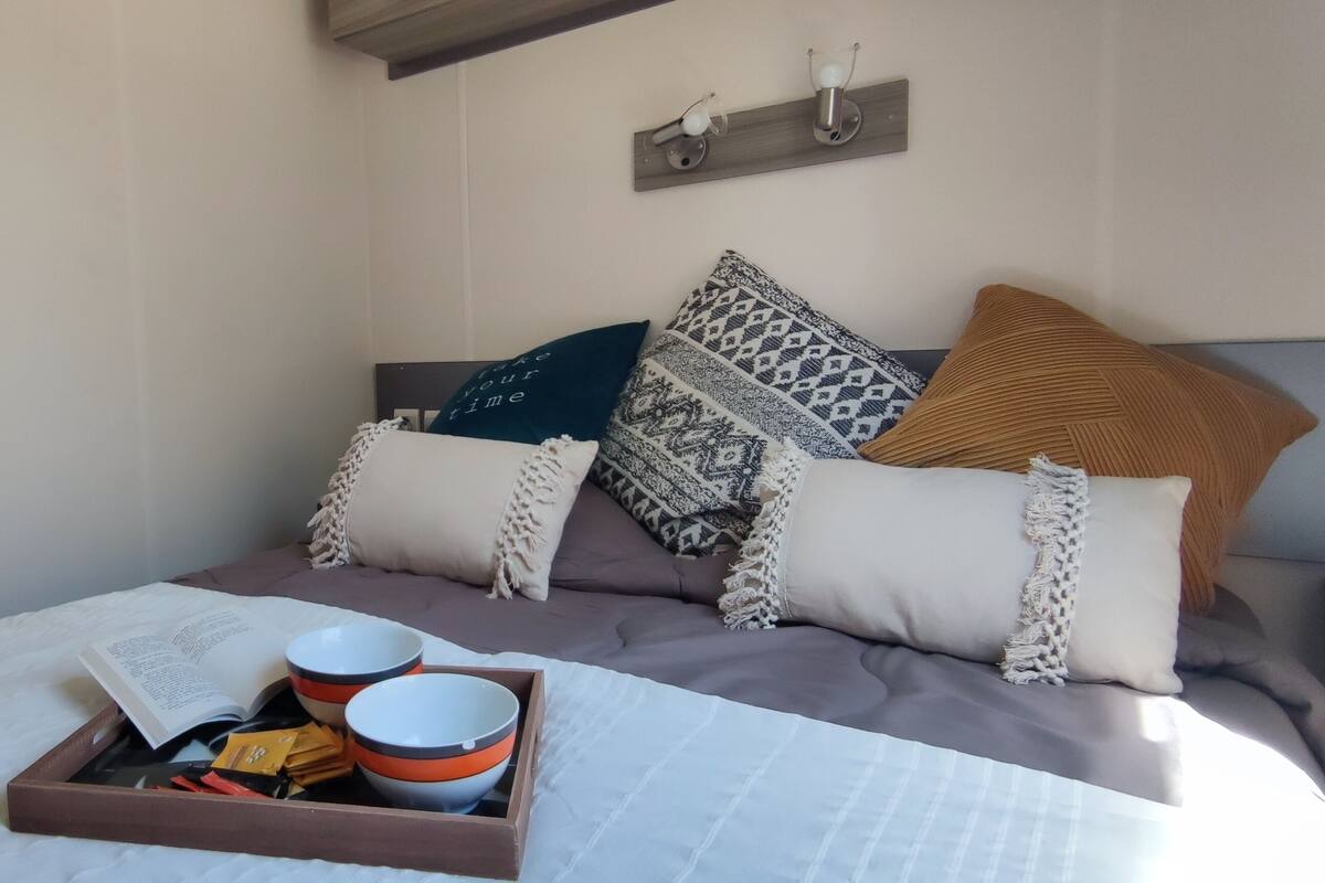 A neatly made bed with a tray of items, including a book and bowls, in a room with a simple, clean design and a wooden headboard.