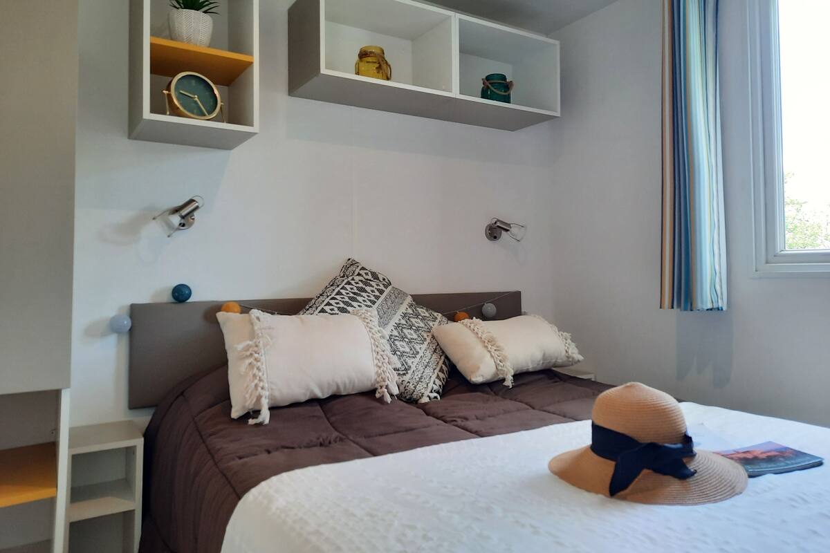A bedroom with a bed, a nightstand, a shelf with decorative items, and a window with curtains.