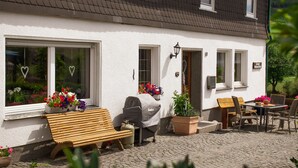 A white building with a black roof, a wooden bench, a table with chairs, and potted plants. - Bauernhof Pension Wiebelhaus Mester (Lennestadt)