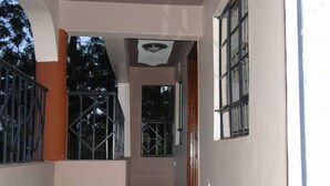 A corridor with a tiled floor, a ceiling light, and a window with metal bars. - Easy Sleep Guesthouse (Kitale)