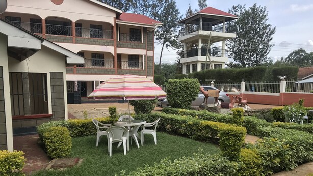 A multi-story building with a balcony, a small garden with a table and chairs, and a statue of a camel. - Easy Sleep Guesthouse (Kitale)