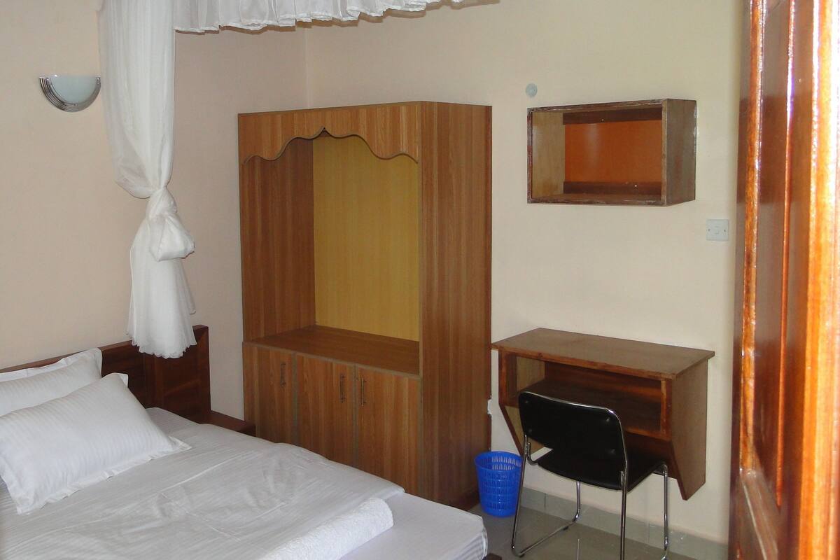 Une chambre à coucher avec un lit, une armoire en bois, un bureau, une chaise et un petit miroir.